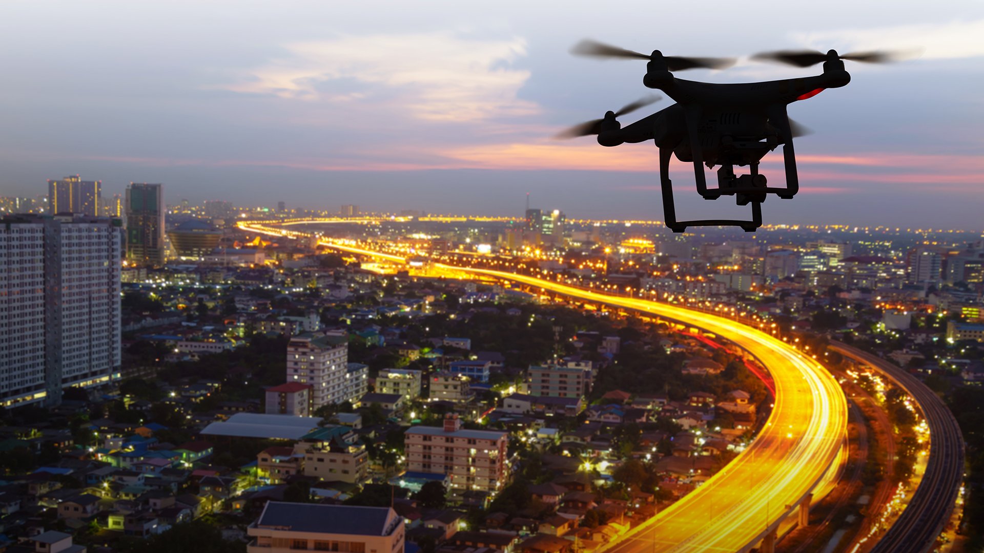 Silhouette of drone flying above city at sunset