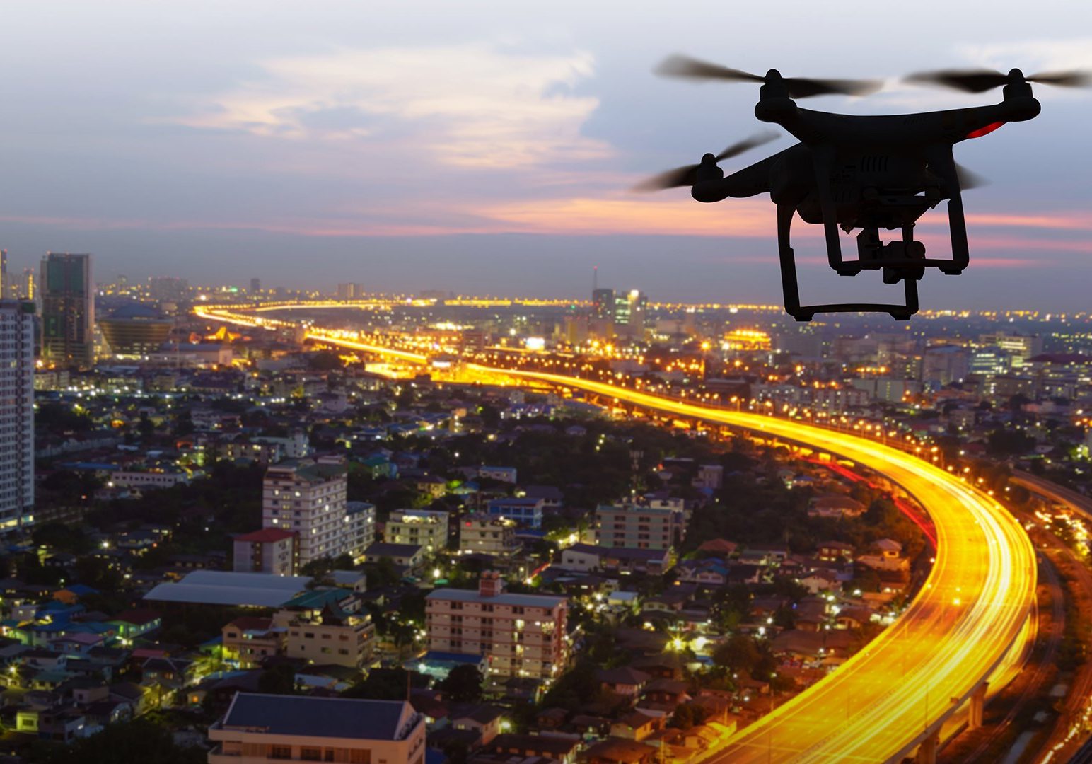 Silhouette of drone flying above city at sunset